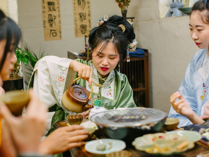 Three women in traditional Chinese dress at a tea tasting ceremony